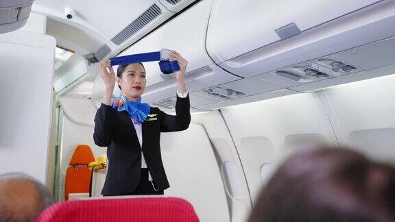 美丽的亚洲空姐制服展示如何使用安全带和其他安全措施的航班上的乘客在客舱在飞机上