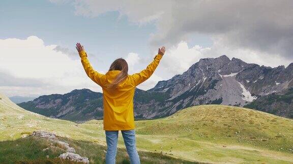 年轻快乐的女子在黄色雨衣举起手欣赏美丽的山慢镜头