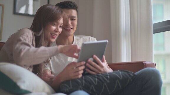 一对亚洲中国年轻夫妇周末一起在客厅看数字平板电脑