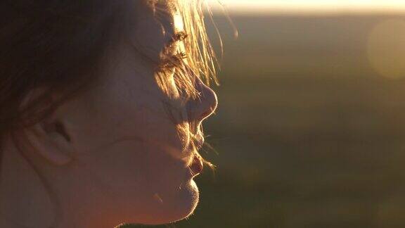 一个年轻美丽的女人看着夕阳的脸风吹动了她的头发