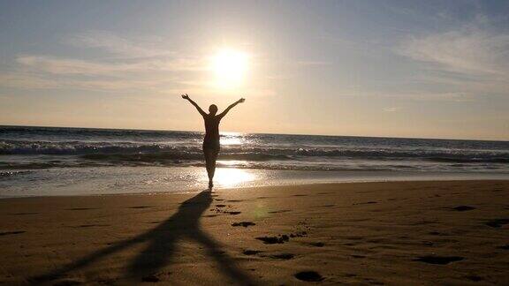 一位年轻女子在日落时分跑到海边举起手美丽的年轻女孩在沙滩上去海边享受假期的自由暑假放松一下后方后视图