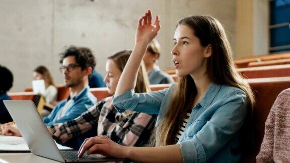 年轻漂亮的学生在大学听讲座时使用笔记本电脑她举手向讲师提问现代聪明学生的多民族群体
