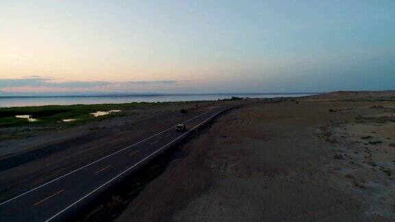 日落时分汽车在沙漠中间的空旷道路上行驶的