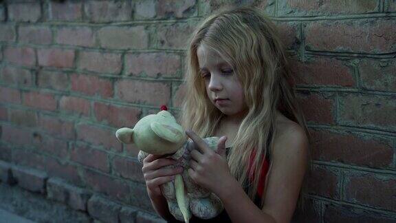 一个来自贫困家庭的蓬头垢面的小女孩在一堵砖墙前玩着她的玩具