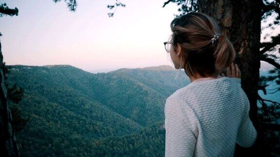 一个戴眼镜的小女孩站在悬崖边看着青山从后面看穿越群山