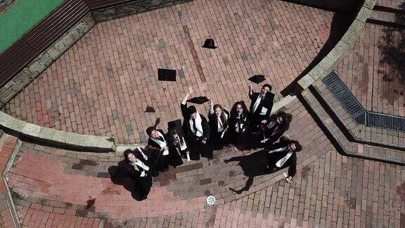 快乐的拉丁美洲学生把毕业帽抛向空中在大学校园里庆祝