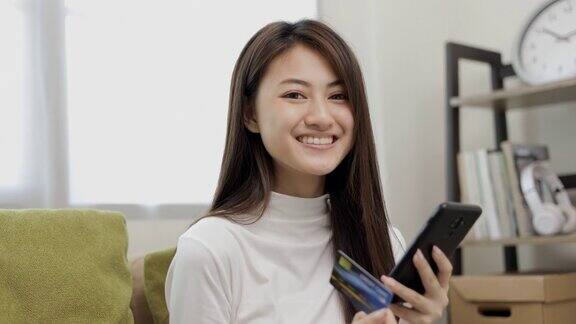 网上购物一名年轻的亚洲少女将信用卡序列号输入智能手机进行购物支付购买网上送货上门的物品微笑的女性感觉快乐