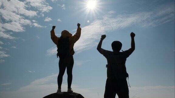 一对成功的亚洲夫妇在山顶举起手臂欣赏日落前的山谷景色