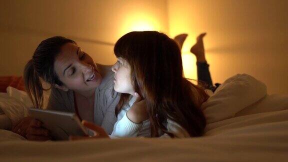 母亲和女儿躺在家里的床上用电子平板电脑看东西