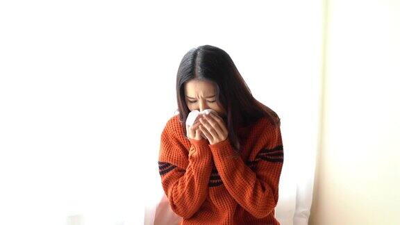 生病的亚洲妇女坐在家里靠窗的椅子上用餐巾擤鼻涕患流感或感冒一名亚洲妇女在冬天患流感感冒的女人