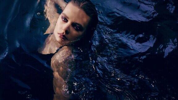 迷人的女人从黑暗中浮现在水面上摇摆关注美丽的皮肤和长发奢华的美容护理
