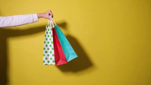 购物或销售概念女人手里拿着很多购物纸袋孤立在黄色的背景上视频横幅与复制空间手贪婪地拿起纸袋