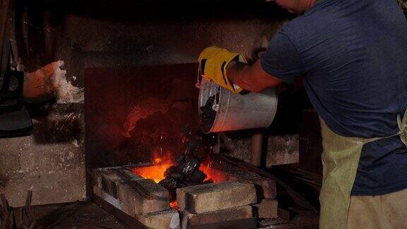 一名男铁匠将无烟煤倒进铁匠铺的篝火中