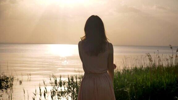 年轻快乐的女孩站在海边举起双手抚摸头发转身阳光剪影50帧