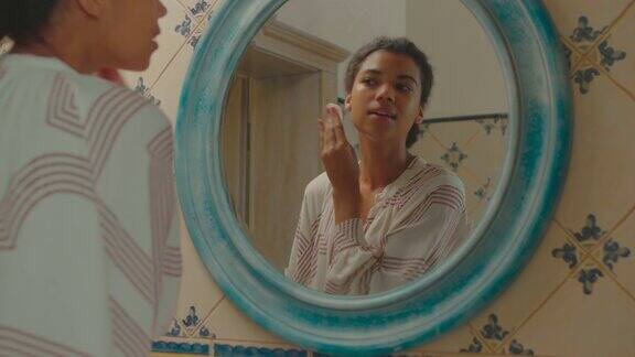 近距离的年轻成年非洲裔美国妇女清洁她的脸皮肤与白棉垫看着镜子在浴室女性在家里卸妆