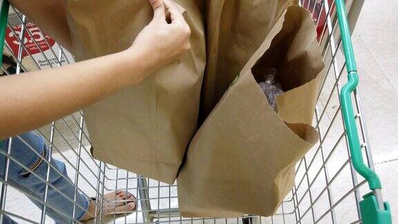 一个女人把装在纸袋里的杂货装进购物车