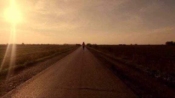 鸟瞰图的年轻女子奔跑在农村道路上的日落