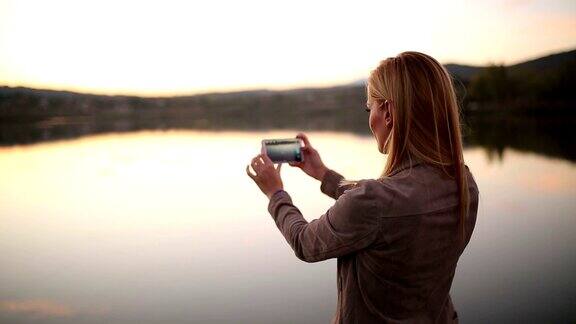在日落时用手机拍照的女人