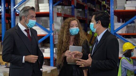高级商务人员和女秘书戴着防护医用口罩在大仓库与亚洲仓库经理交谈业主陪同主管参观工厂并进行检查