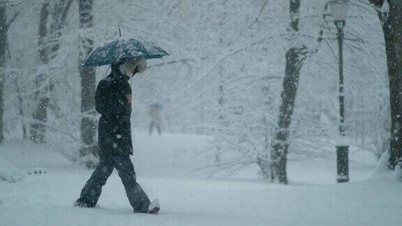 慢镜头:一个女人穿着冬衣拿着雨伞穿过暴风雪