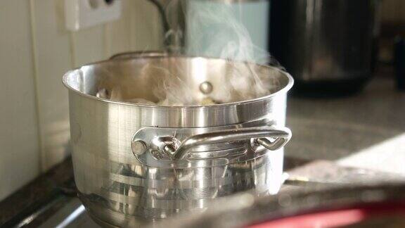 平底锅在煤气炉上用蒸汽喷射上升在厨房的电炉上用蒸汽锅烧水模糊的背景烹饪煤气炉上的锅厨房里蒸锅的特写