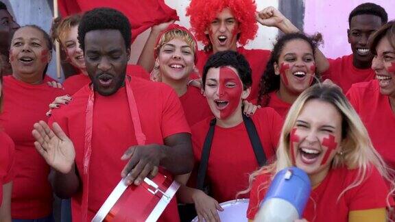 ▽在体育场观看足球比赛的多种族球迷=身穿红色t恤的人们在体育世界锦标赛上享受着兴奋的乐趣
