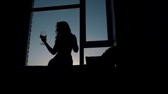 跳舞的女士拿着酒杯靠在窗户上的剪影