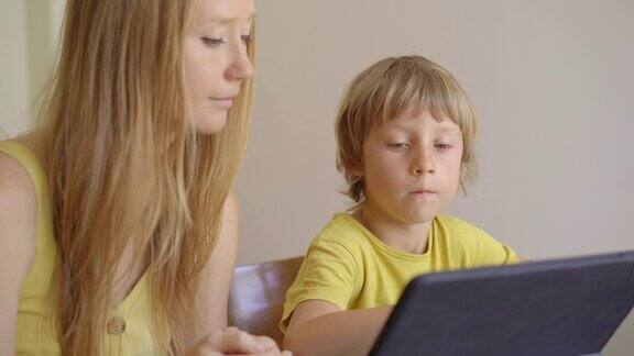 一位年轻妇女和她的小儿子在隔离期间坐在家里在互联网学校使用平板电脑学习冠状病毒