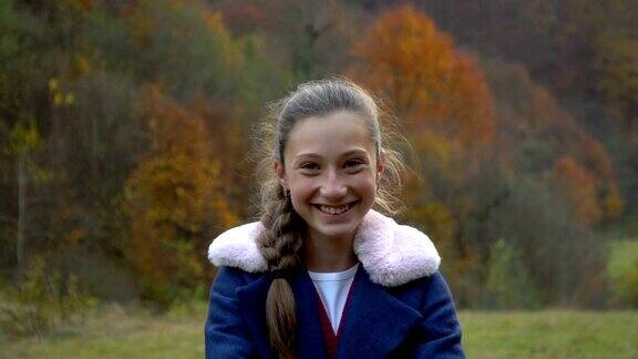 一个美丽的年轻女孩站在秋天的森林里看着相机微笑着她是快乐的缓慢的运动
