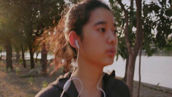 迷人的亚洲少女听音乐同时在公园里跑步年轻女子晨跑锻炼
