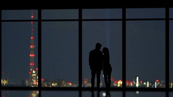 一对年轻夫妇站在窗前欣赏城市夜景