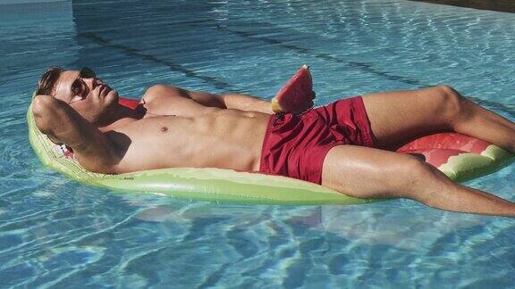 一个年轻人睡在游泳池里的西瓜充气上