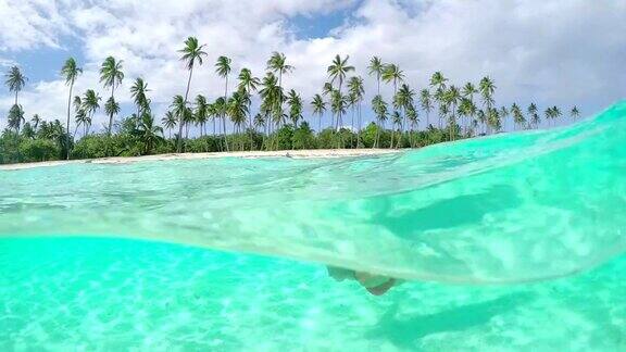 4K慢镜头水下近距离:快乐的年轻女子放松和游泳在完美的蓝色泻湖在热带岛屿与异国情调的白色沙滩和棕榈树在她的暑假