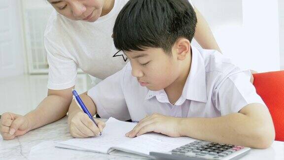 亚洲母亲在白色桌子上帮助儿子做作业的慢镜头严肃的亚洲母亲和儿子在客厅做作业妈妈教儿子如何成为天才