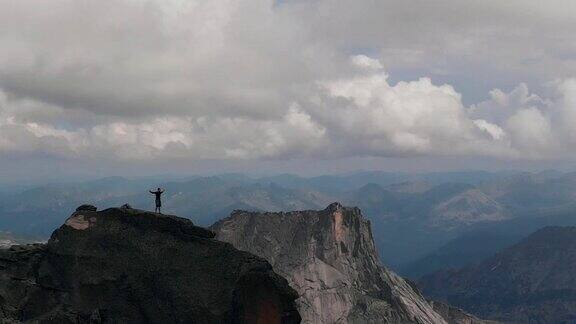 一个男人站在山顶的航拍照片年轻的登山者爬完山高兴地举起了手