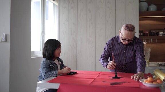 亚洲华人祖父和孙女在中国新年庆祝期间练习书法家里装饰一张红色的纸