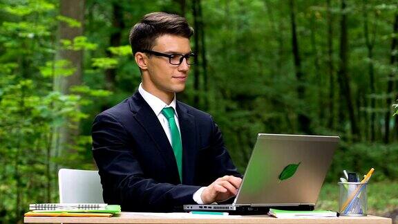 年轻的办公室职员坐在绿色的公园里用笔记本电脑打字动作缓慢