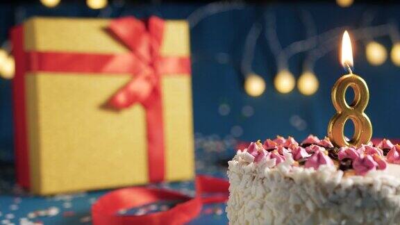 8号白色生日蛋糕金色蜡烛用打火机点燃蓝色背景用彩灯和黄色礼盒用红丝带绑起来特写镜头