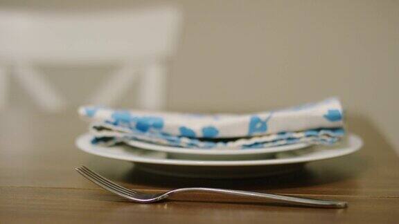 白种人女人的手把叉子放在白色餐盘的左边木桌上有白色沙拉盘和彩色的花布餐巾