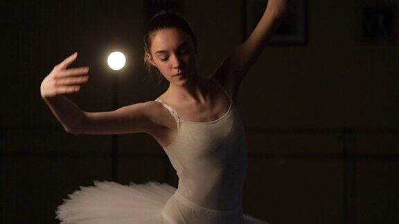 一位优雅的芭蕾舞演员在黑暗中以灯光为背景慢动作地跳着芭蕾元素