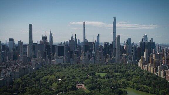 空中直升机镜头在中央公园与自然树木人们野餐和休息在曼哈顿摩天大楼周围的田野景观美丽的晴天