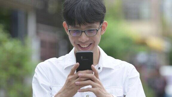 年轻快乐的亚洲商人微笑着在户外的街道上使用电话