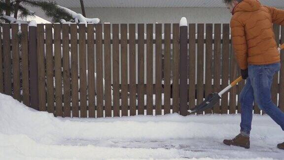 一个男人用雪铲从篱笆附近的路上铲雪