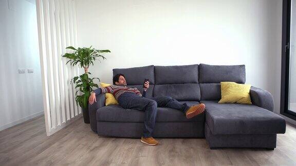 在美丽的家里白人男子躺在沙发上使用智能手机