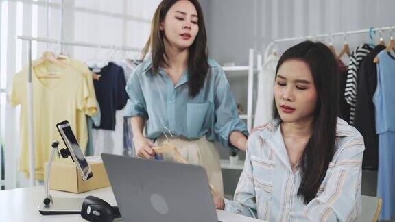 亚洲女性企业主在时装商店展示服装在智能手机前录制视频视频直播向顾客出售时装网上购物概念