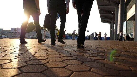 三个商人的脚走在机场附近太阳耀斑的背景一群面目全非的商人一起去码头自信的人正在上班的路上同事去户外慢动作特写后视图