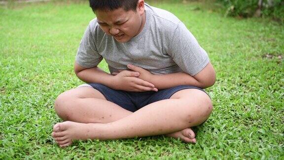 肥胖的胖男孩坐在草坪上忍受着胃痛因为食物中毒