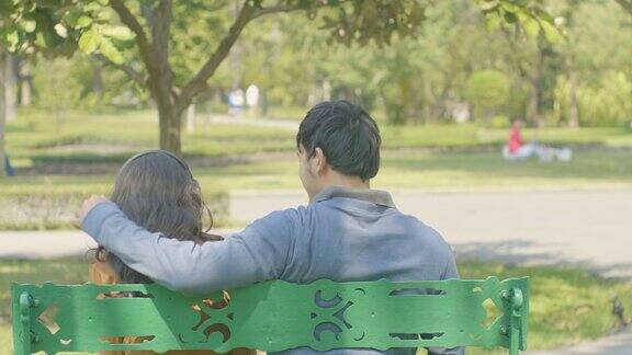 快乐的年轻夫妇在公园的长椅上放松从后面拍摄爱