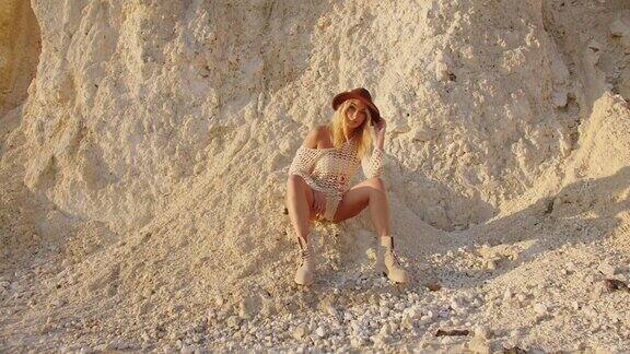 一个可爱的金发模特坐在岩石中间在一个炎热的阳光灿烂的日子里拍摄照片