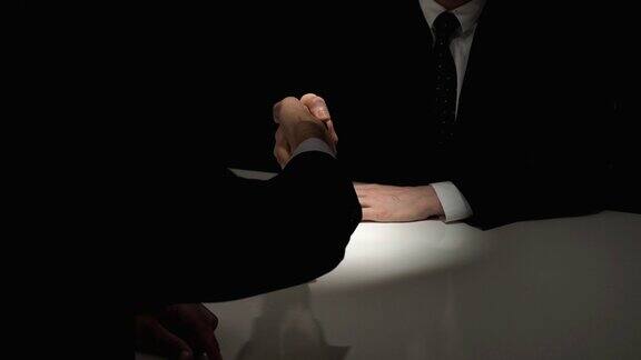 在暗室里的秘密会议上匿名的商业伙伴握手